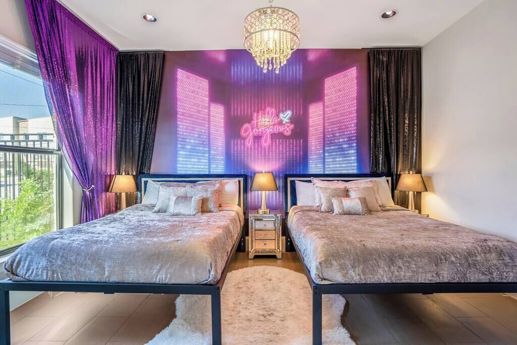 Een slaapkamer met twee bedden, een kroonluchter en een neonbord aan de muur.