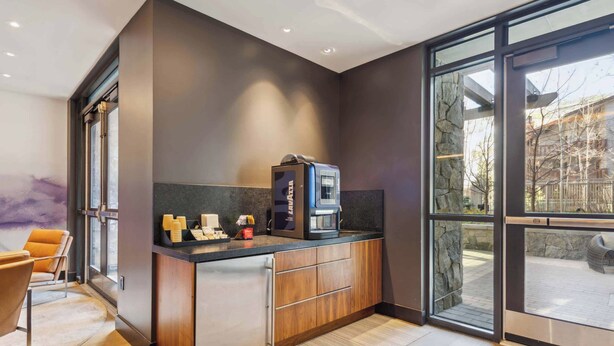 A modern kitchen with a built-in coffee machine, wooden cabinets, and a large window offering a view of the outdoors.