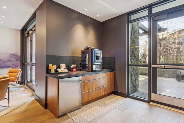 A modern kitchen with a built-in coffee machine, wooden cabinets, and a large window offering a view of the outdoors.