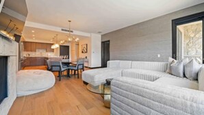 A modern living room with a sectional sofa, a dining area with a table and chairs, and a kitchen in the background.