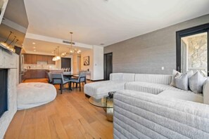 A modern living room with a sectional sofa, a dining area with a table and chairs, and a kitchen in the background.