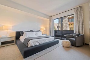 A modern hotel room with a large bed, a sofa, a small table, and a view of the outside.