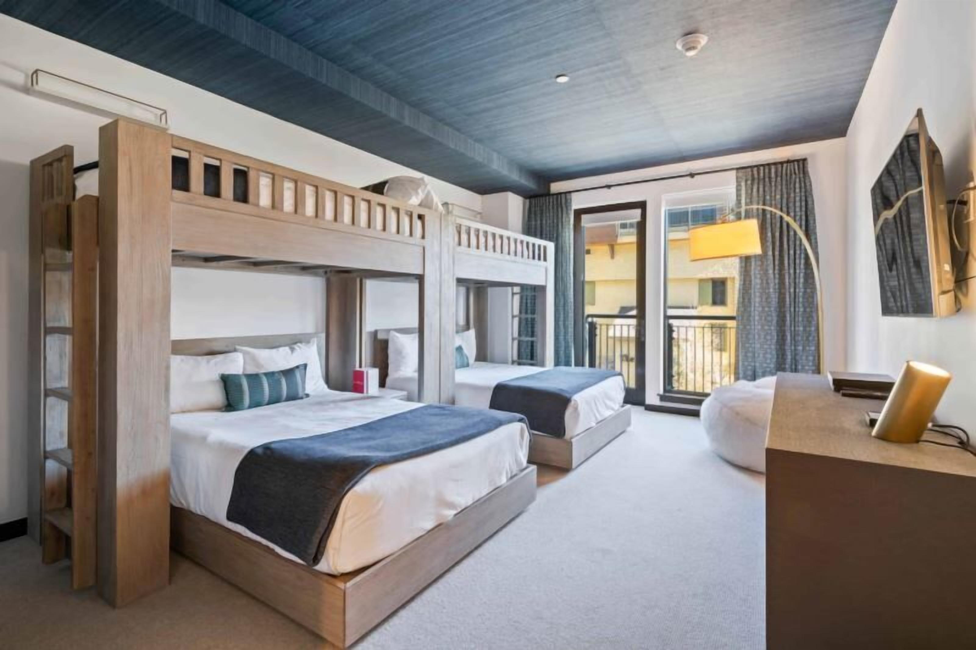 Une chambre d’hôtel avec des lits superposés, un bureau et un balcon avec des rideaux.