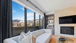 A modern living room with a large window, a sofa, a fireplace, and a view of the city.