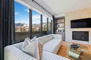A modern living room with a large window, a sofa, a fireplace, and a view of the city.