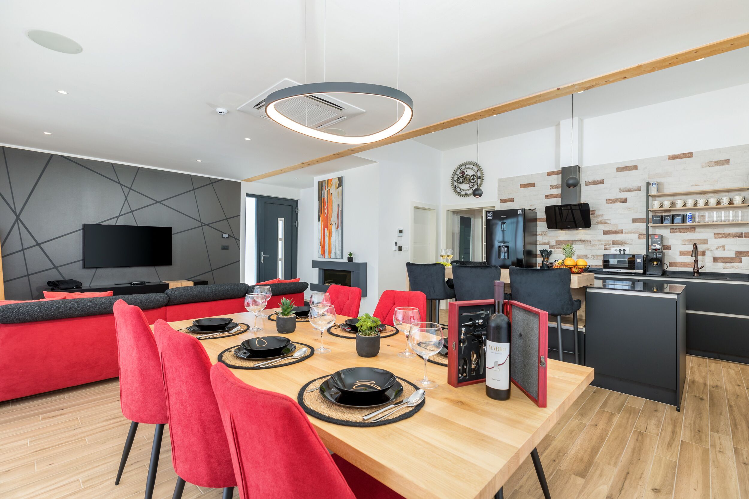 Une cuisine moderne avec un coin repas, comprenant une table en bois dressée pour quatre personnes, des chaises rouges et un ensemble de vaisselle noir.