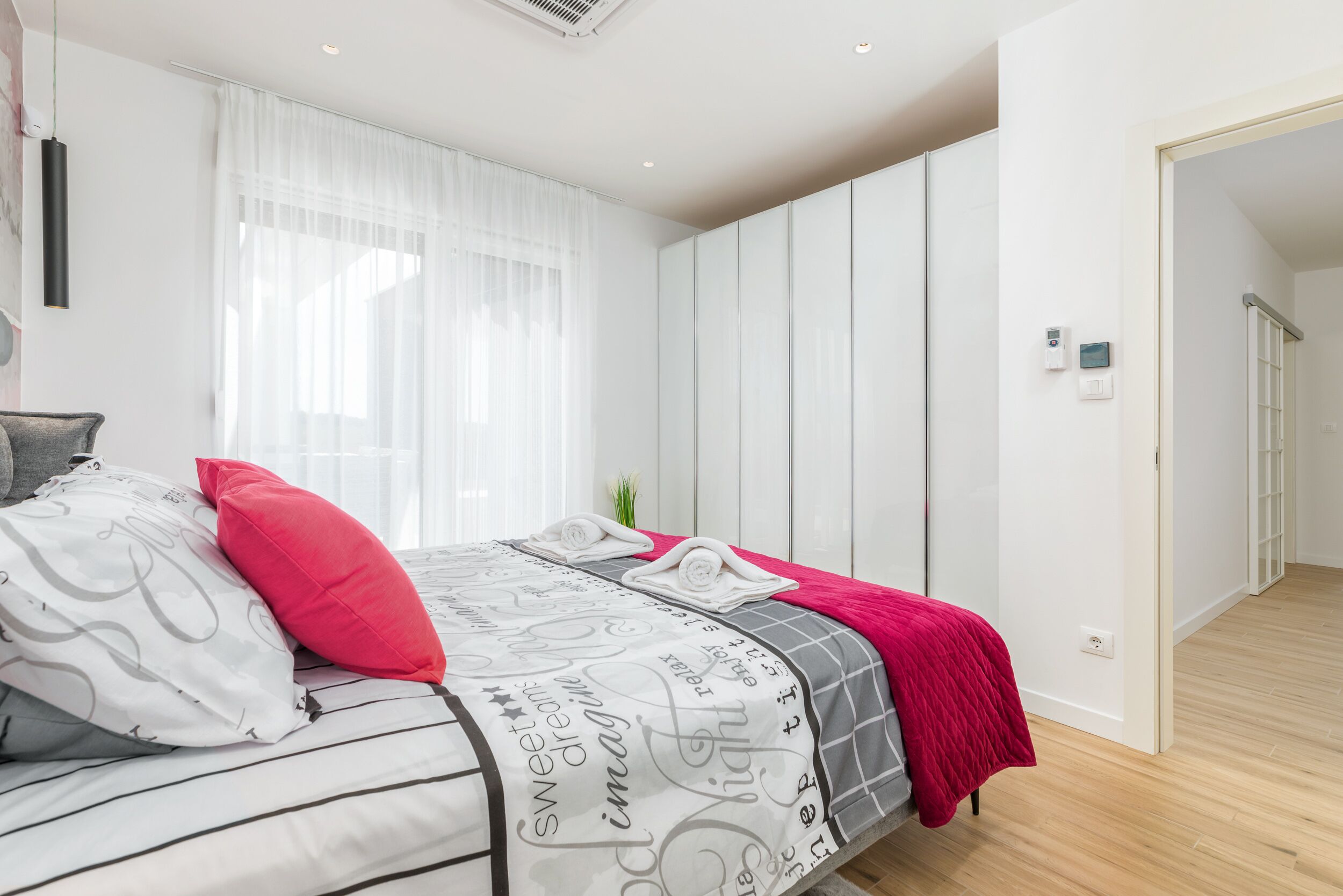 A modern bedroom with a bed, pillows, and a red throw blanket.