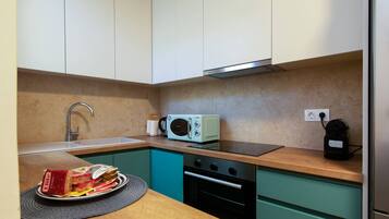 A compact kitchen with teal cabinets, a microwave, a sink, and a small oven.