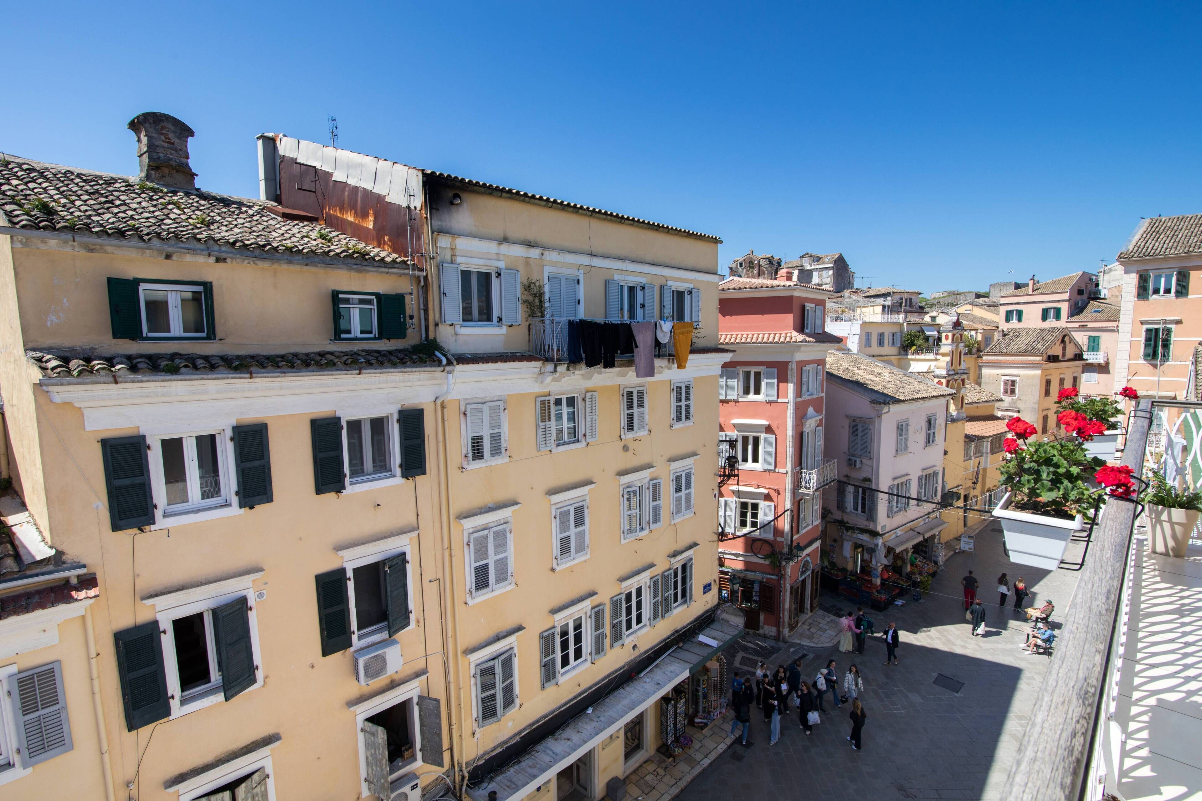 Um edifício com várias andares e sacadas, uma rua para pedestres e um céu azul claro.