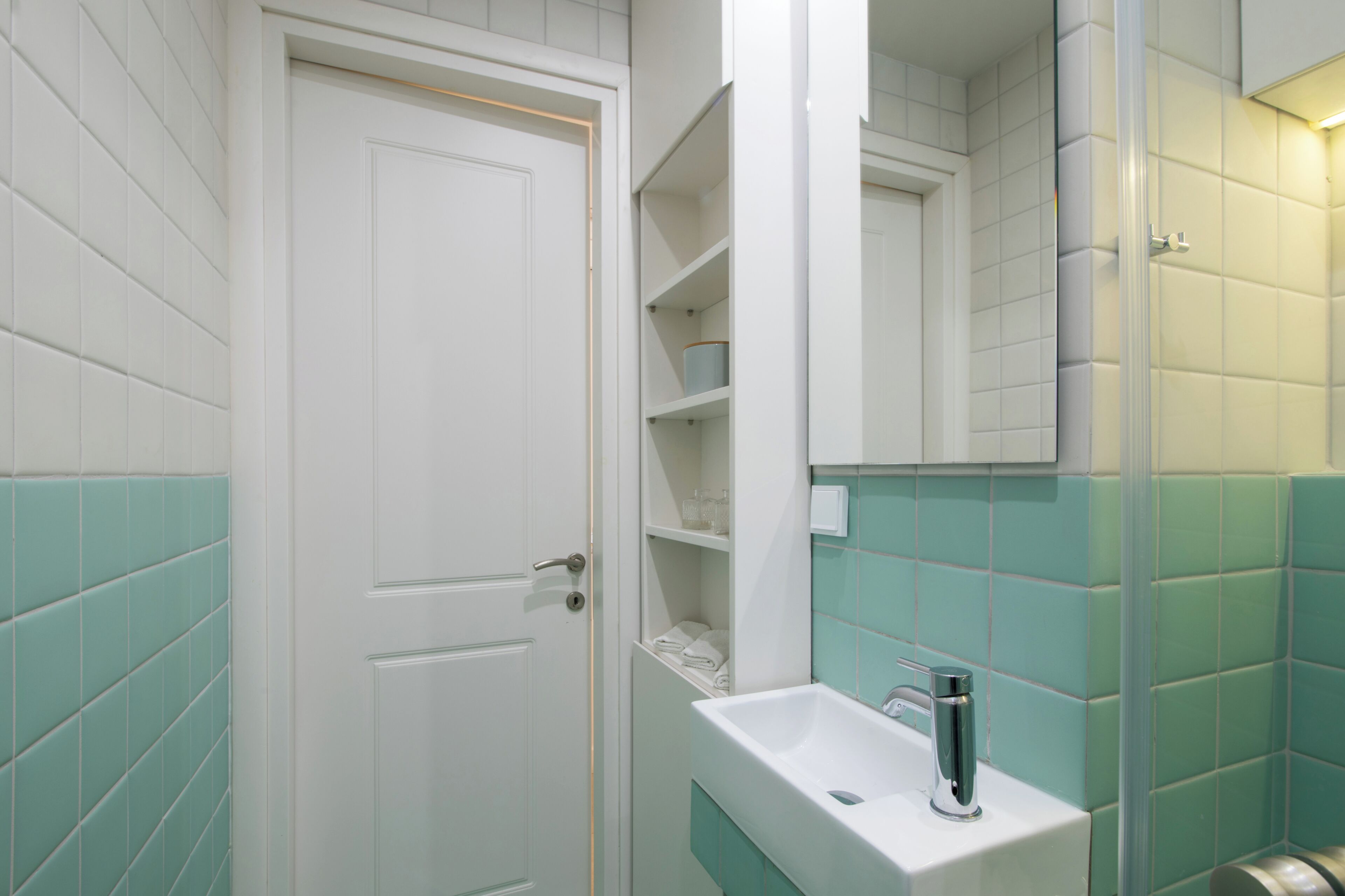 A bathroom with a white door, a sink with a faucet, and shelves with toiletries.