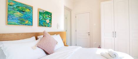 Ein Schlafzimmer mit einem hölzernen Kopfteil, weißer Bettwäsche, zwei Bildern an der Wand und einem Kleiderschrank.