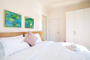 Un dormitorio con cabecera de madera, ropa de cama blanca, dos cuadros en la pared y un armario.