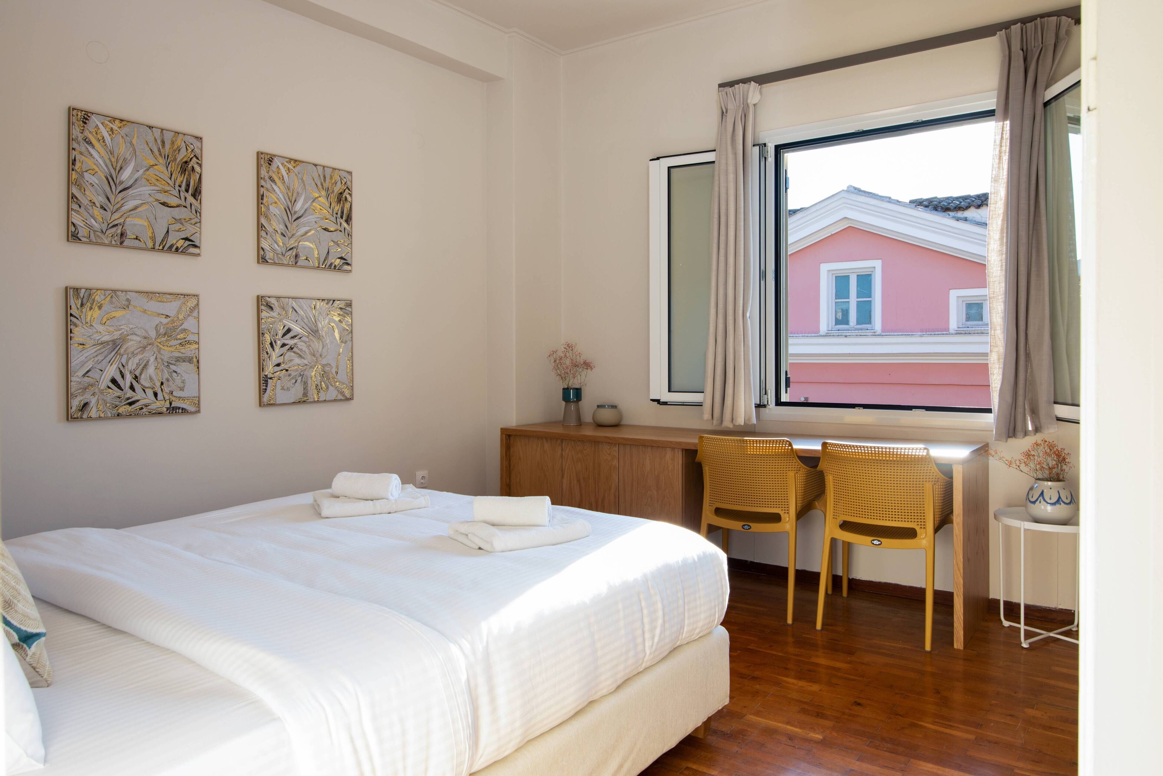 A bedroom with a bed, two chairs, a desk, and a window with curtains.