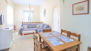 A cozy living room with a sofa, a dining table with chairs, a television, and a window with a view of trees. - Vista Mare Ilios in Nisaki (Corfu)