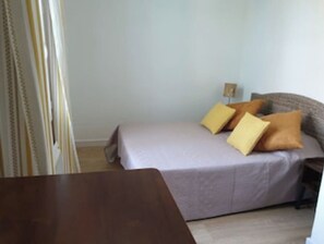 Un dormitorio con cama, almohadas, una mesita de noche y una mesa de madera.