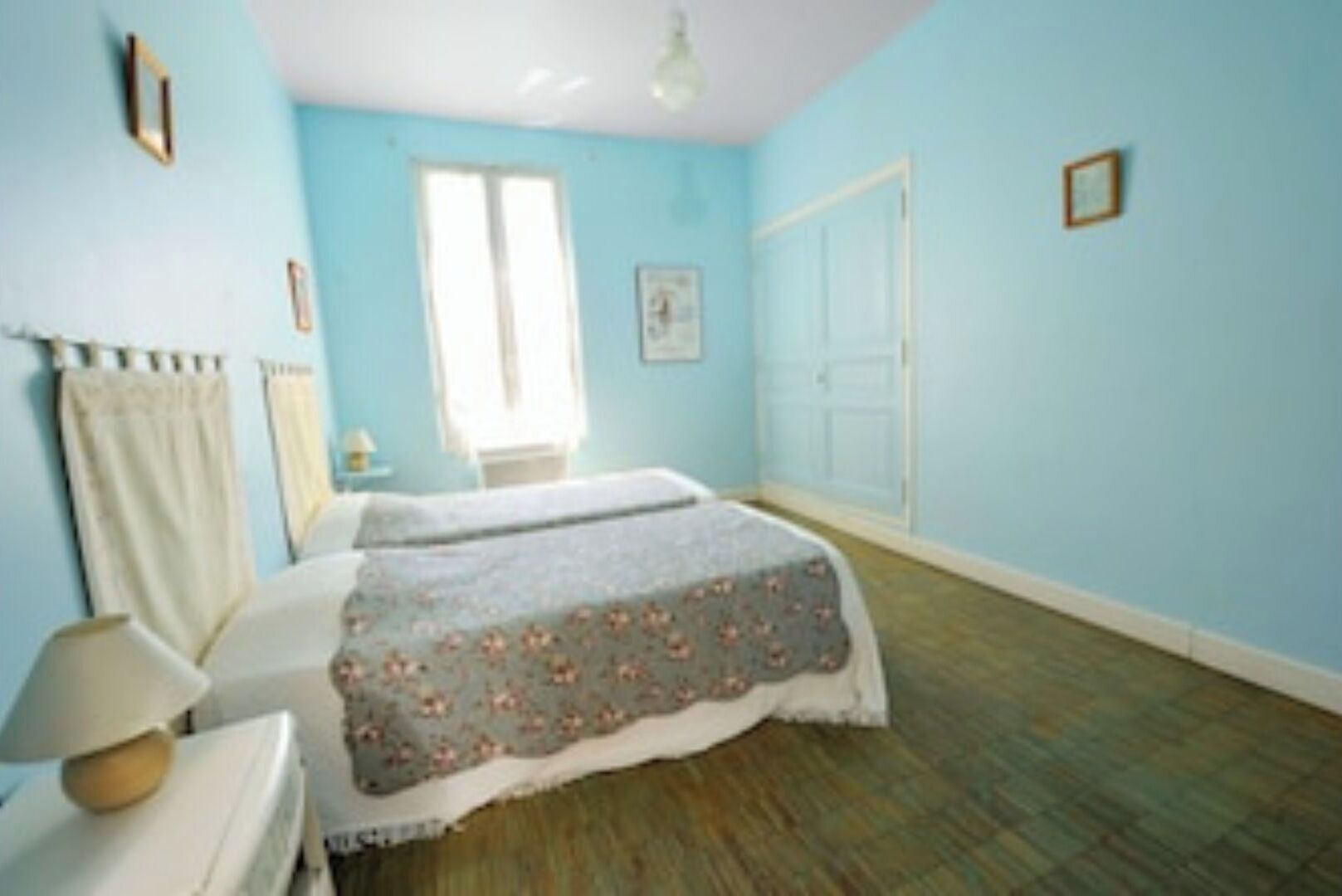 A bedroom with a bed, a bedside table, a lamp, a window, and a door.