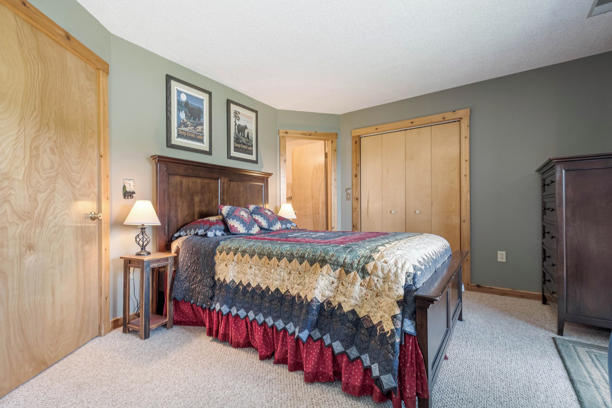 Une chambre à coucher avec un lit en bois, une table de chevet, une lampe, une commode et deux tableaux encadrés accrochés au mur.