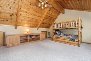 Une pièce avec un plafond en pente, des lits superposés en bois, un bureau avec des rangements et un ventilateur de plafond.