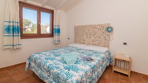 Un dormitorio con cama, cortinas, cabecero y una mesita de noche pequeña.