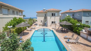 Ein Schwimmbad mit Liegestühlen und Sonnenschirmen, umgeben von Gebäuden im mediterranen Stil.