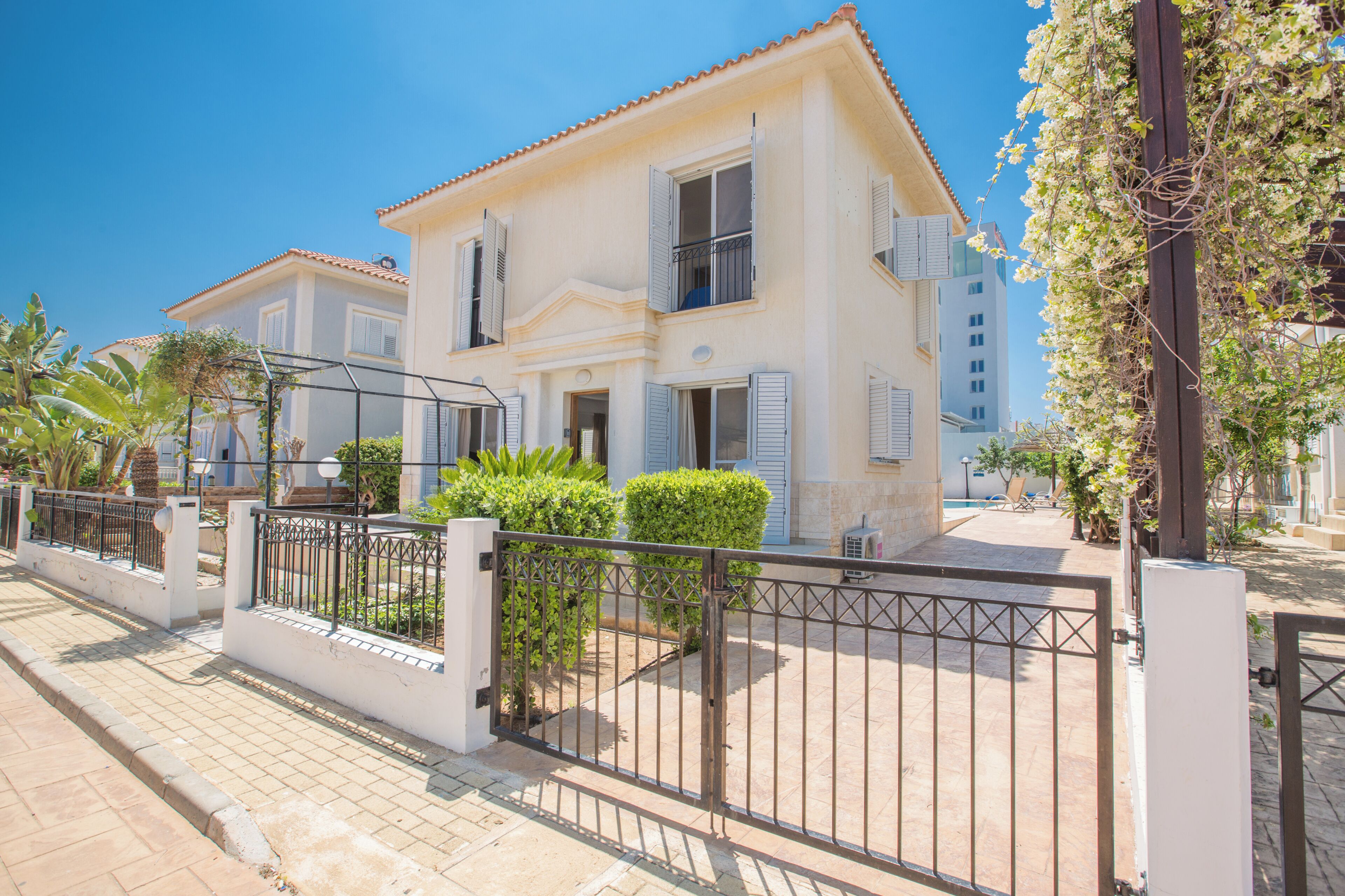 A two-story house with a tiled roof, a gated entrance, and a small garden area.
