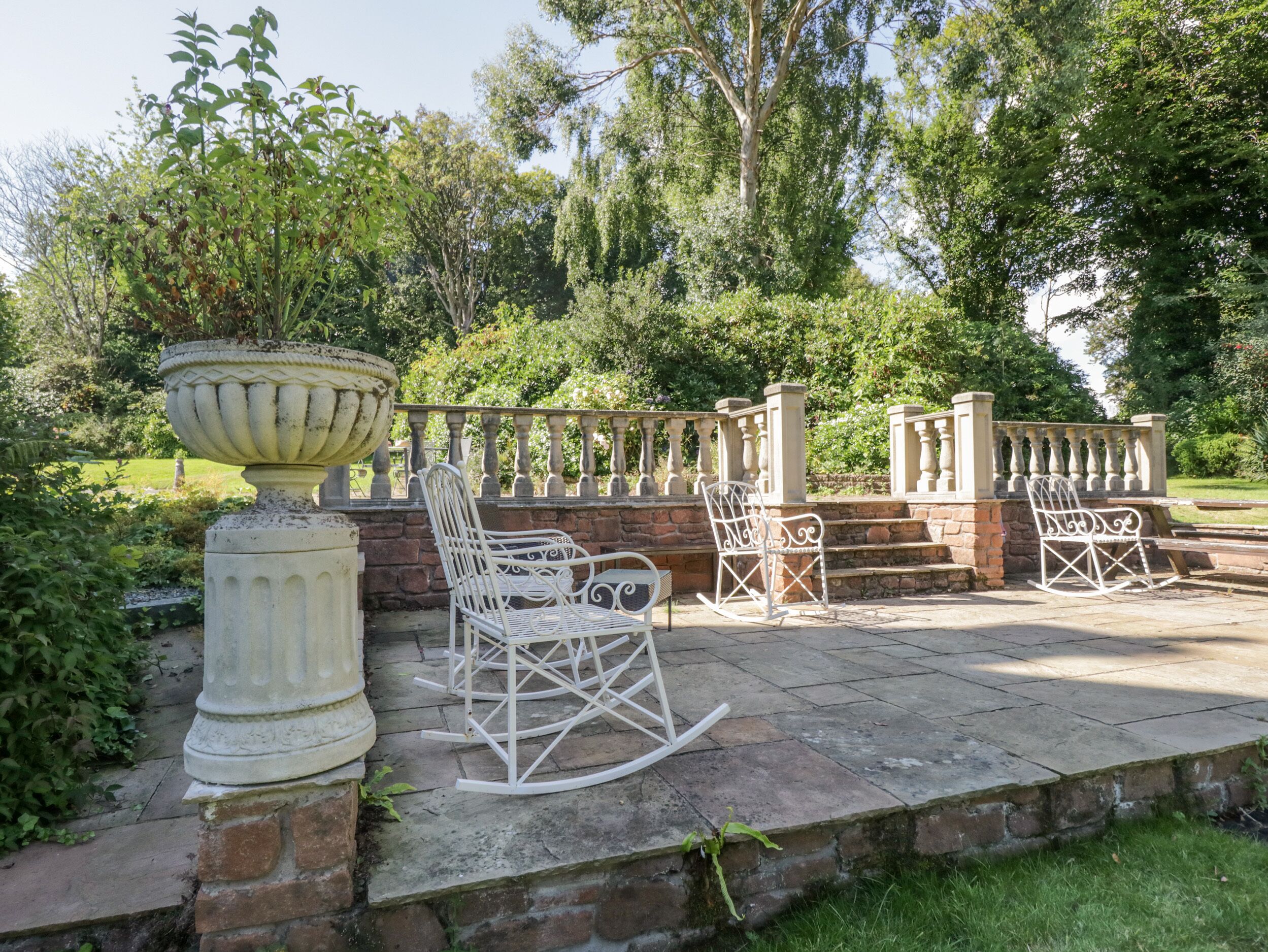 Un espace patio agrémenté d’un bac à fleurs blanc, de deux fauteuils à bascule et d’une balustrade en pierre.