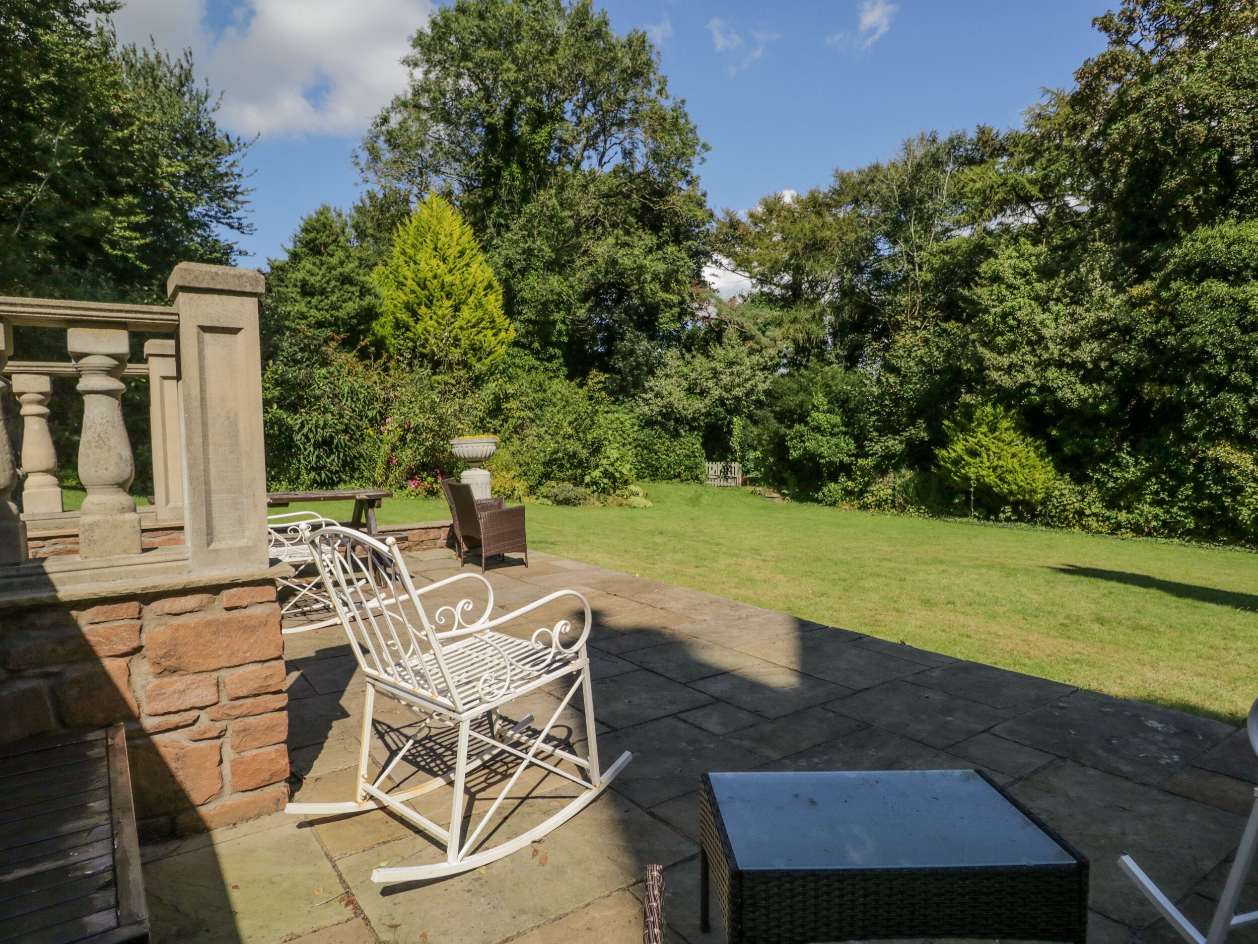 A patio with a white rocking chair, a small table, and a wicker ottoman.