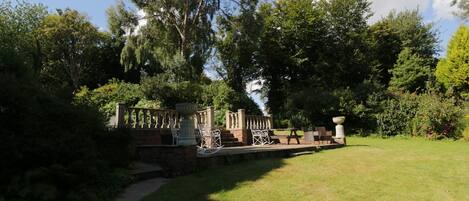 A garden with a stone bridge, seating area, and a large tree.