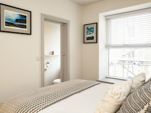 A bedroom with a bed, a window with blinds, a door leading to a bathroom, and two framed pictures on the wall.
