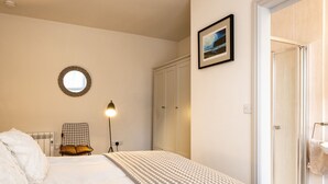 A bedroom with a bed, a bedside lamp, a round mirror, a wardrobe, and a framed picture on the wall. - The Lookout (Wadebridge)
