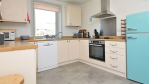 A compact kitchen with white cabinetry, a built-in oven, a microwave, and a blue refrigerator. - The Lookout (Wadebridge)