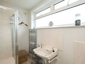 A bathroom with a glass shower enclosure, a white sink with a single faucet, a towel rack, and a window with a view of the sky.