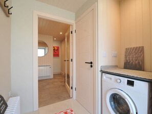 A laundry room with a front-loading washing machine, a radiator, and a mirror. - The Lookout (Wadebridge)