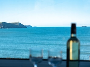 A table with a bottle and two glasses, overlooking a coastal view with cliffs and the sea.