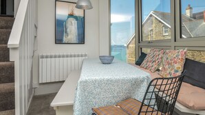 A room with a view of houses through large windows, a white radiator, a bench, a table with a bowl, and a framed picture on the wall. - The Lookout (Wadebridge)