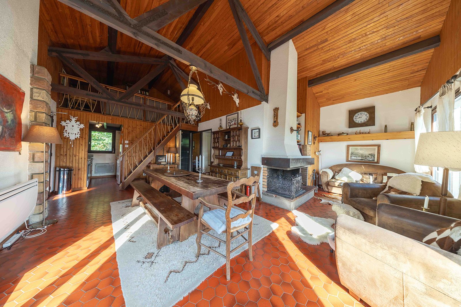 A spacious living area with a wooden staircase, a fireplace, and a dining table.