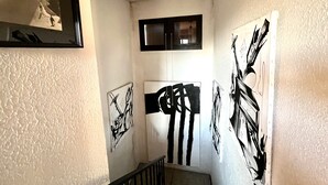 Un pasillo con paredes blancas y texturizadas, una ventana con marco negro y varias obras de arte en blanco y negro.