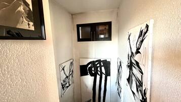 Um corredor com paredes brancas texturizadas, uma janela com moldura preta e várias obras de arte em preto e branco.