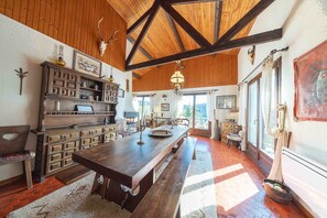 A spacious kitchen with a long wooden table, built-in cabinetry, and a rustic ceiling.