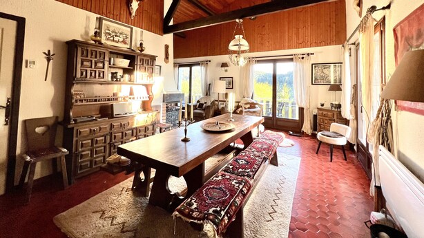 Amplia habitación con techo de madera, una gran mesa de comedor, bancos y vistas al exterior a través de un ventanal.