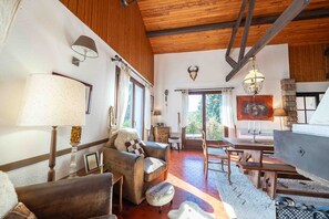 A rustic interior with a wooden ceiling, a dining area with a table and chairs, a sofa, and a fireplace.