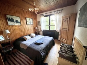 Una habitación acogedora con paneles de madera, una cama con colcha azul, una mesita de noche con lámpara y una ventana con cortinas.