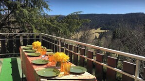 Mesa al aire libre con platos verdes, vasos y flores amarillas, con vista a un valle boscoso.