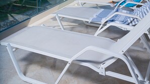 Terraço com cadeiras de lounge brancas e guarda-corpo de vidro com vista para um corpo de água.