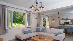 Uma sala de estar moderna com um sofá seccional, uma mesa de centro de madeira e um espaço de jantar com cadeiras azuis.