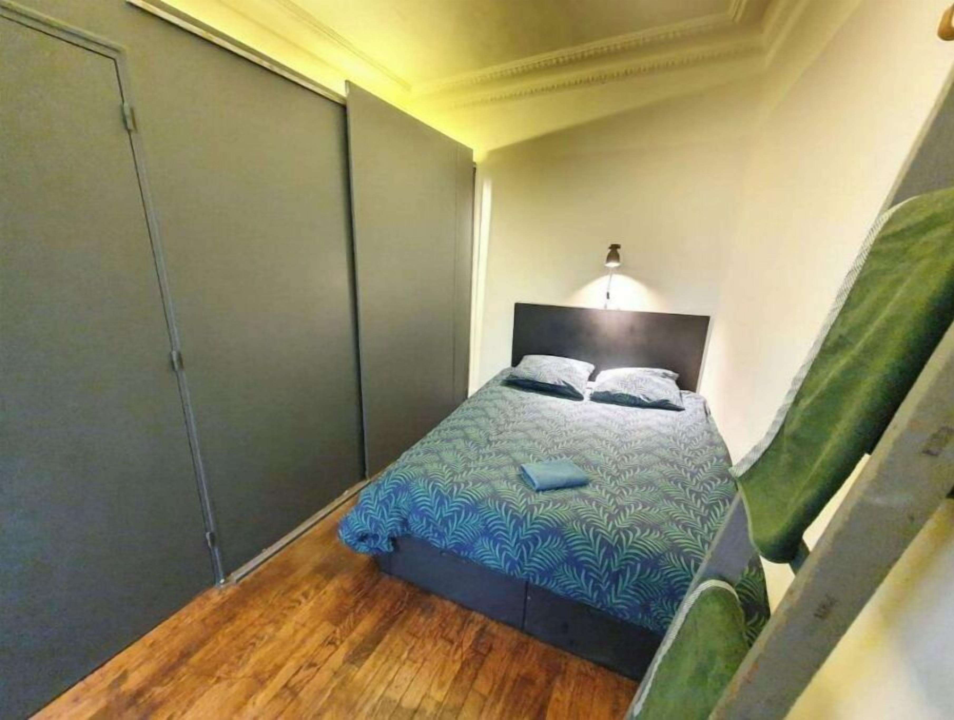 Een slaapkamer met een bed, nachtkastje, lamp en een kledingkast.