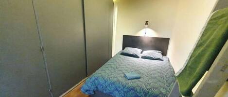 Een slaapkamer met een bed, nachtkastje, lamp en een kledingkast.