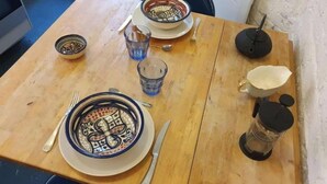 A wooden dining table with a plate, cutlery, a glass, and a thermos.