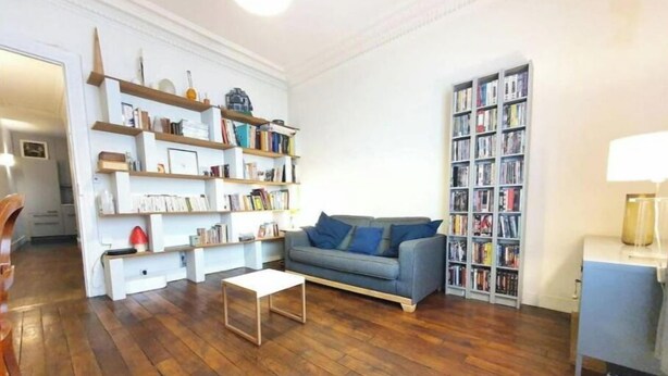 A living room with a grey sofa, wooden flooring, and two bookshelves filled with books.