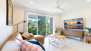 A living room with a sofa, coffee table, TV, and a balcony with a view of greenery.